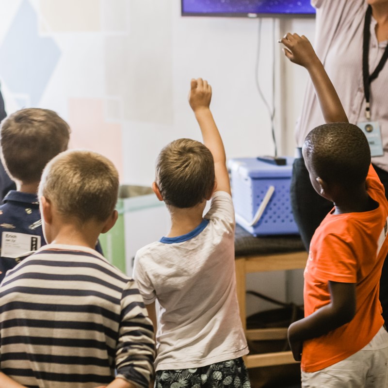 Stock photo of students in a classroom raising their hands.